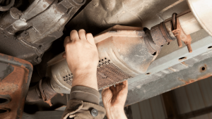 person grabbing catalytic converter underneath vehicle