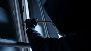 burglar wearing a hoodie and mask attempting to use a crowbar to break in through a door