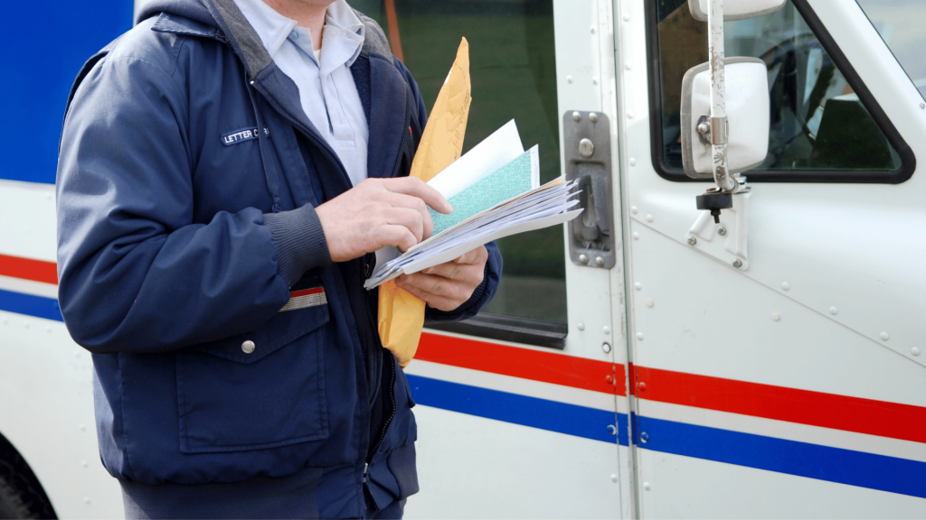 postal carrier holding a stack of mail in front of a USPS truck