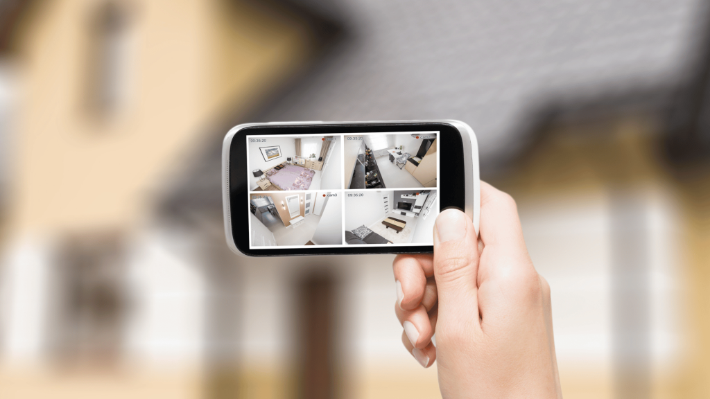 person holding a smartphone with camera feeds in front of a house