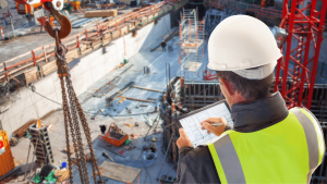 a construction worker writing notes on a tablet and overlooking a work site