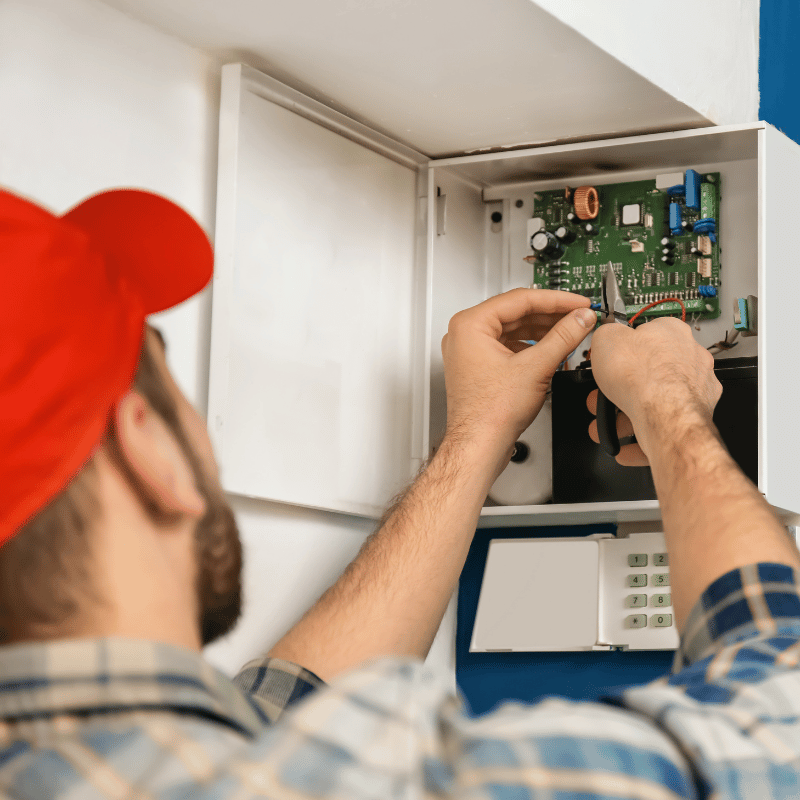 technician looking at wires on a burglar alarm control panel