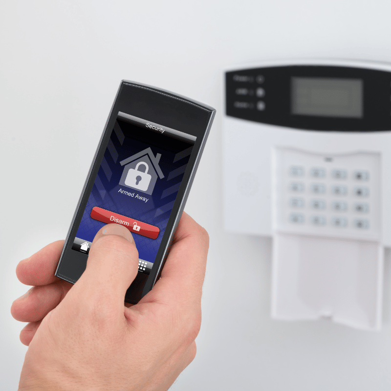 person disarming their burglar alarm system on their phone in front of a keypad mounted on the wall