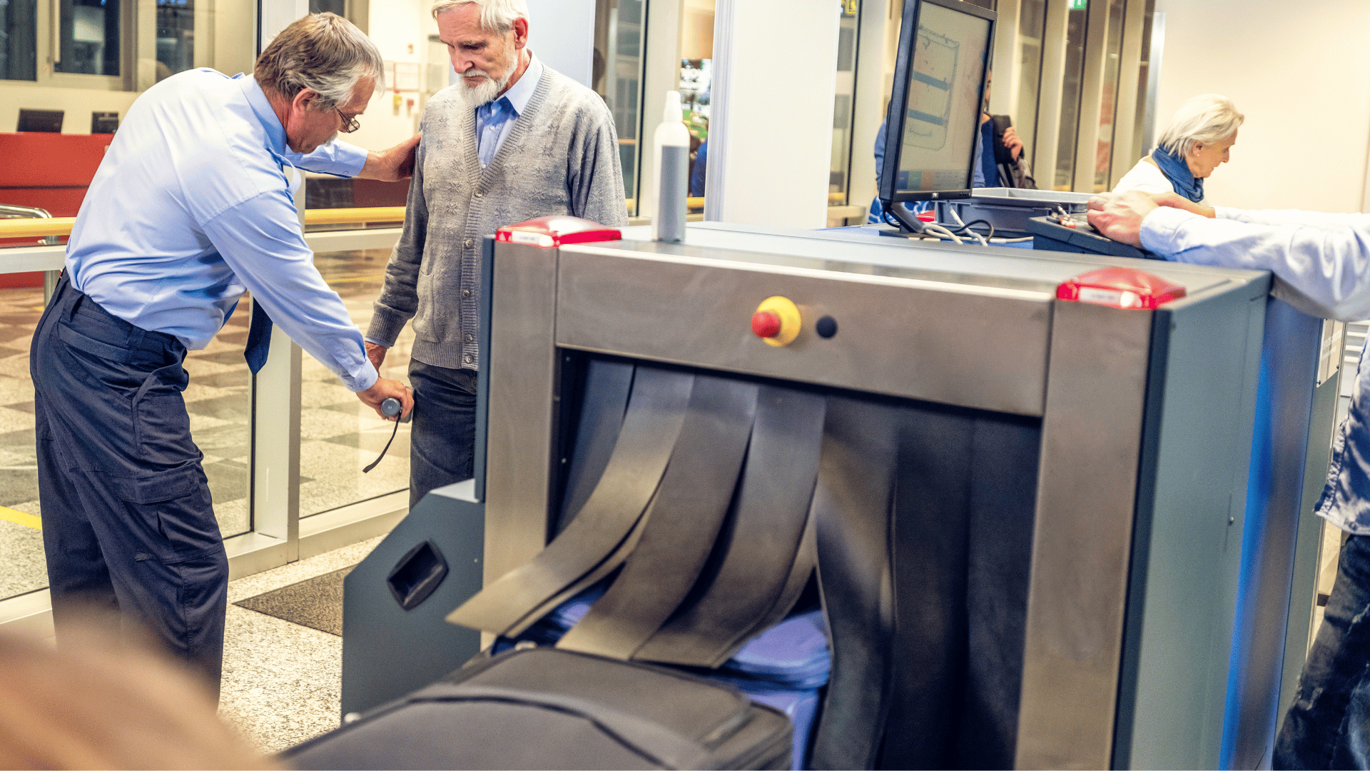 luggage going into x-ray machine at airport security checkpoint with officer checking a man with hand held metal detector in the background