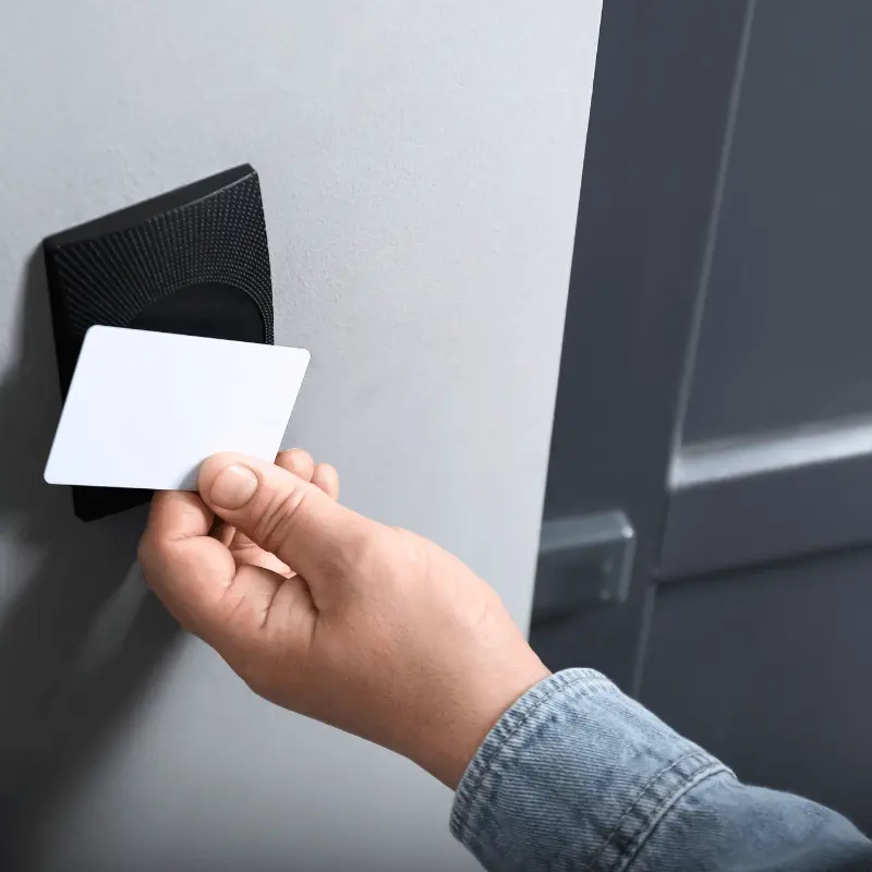 person holding up access card to card reader in front of a door