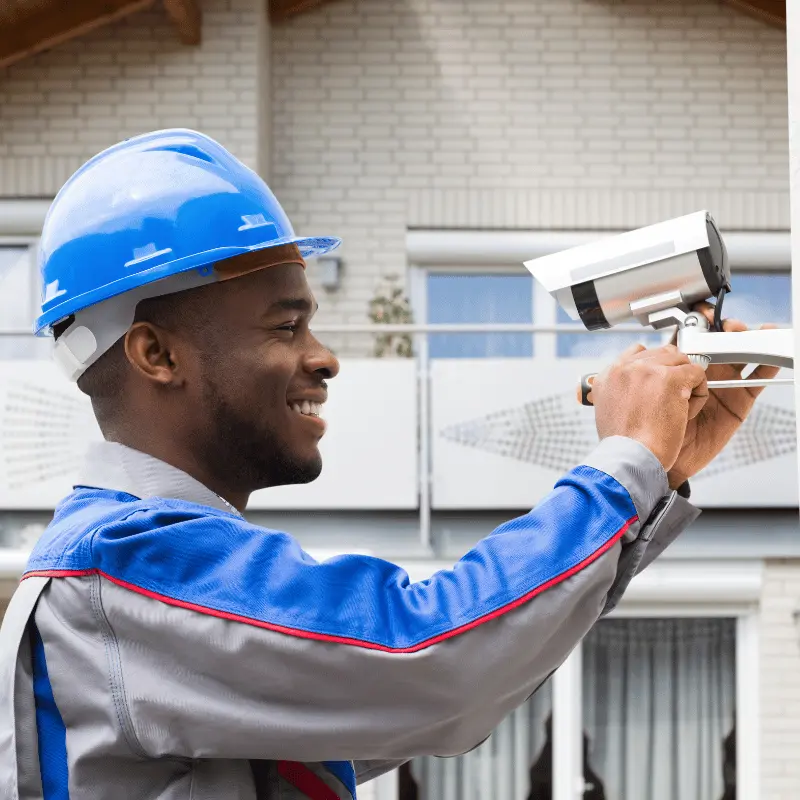 technician smiling as he mounts a security camera outside a building