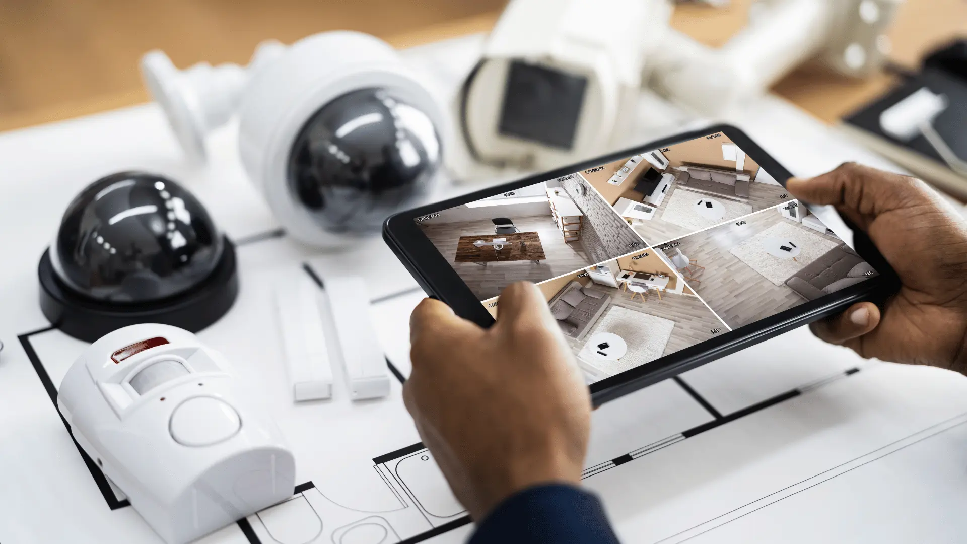 person at a table with security cameras and holding a tablet with camera feeds